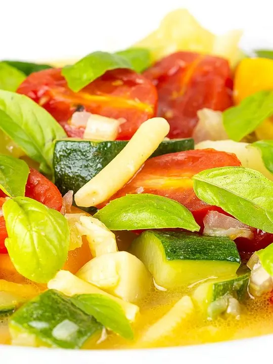 Portrait close up image of a summer vegetable soup featuring courgettes, tomato and new potatoes