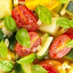 Portrait overhead close up image of a summer vegetable soup featuring courgettes, tomato and new potatoes