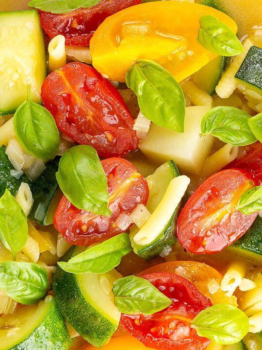 Portrait overhead close up image of a summer vegetable soup featuring courgettes, tomato and new potatoes