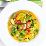 Portrait overhead image of a summer vegetable soup featuring courgettes, tomato and new potatoes served in a white shallow bowl