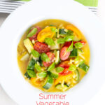 Portrait overhead image of a summer vegetable soup featuring courgettes, tomato and new potatoes served in a white shallow bowl with text overlay