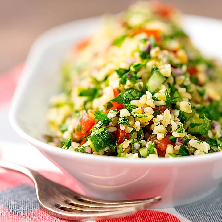 Square image of a herby tabbouleh salad served in a white bowl