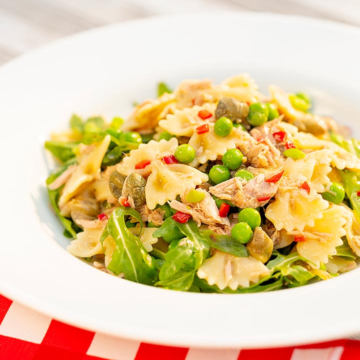 Square image of a tuna pasta salad with peas, chilli and rocket (arugula) served in a shallow white bowl