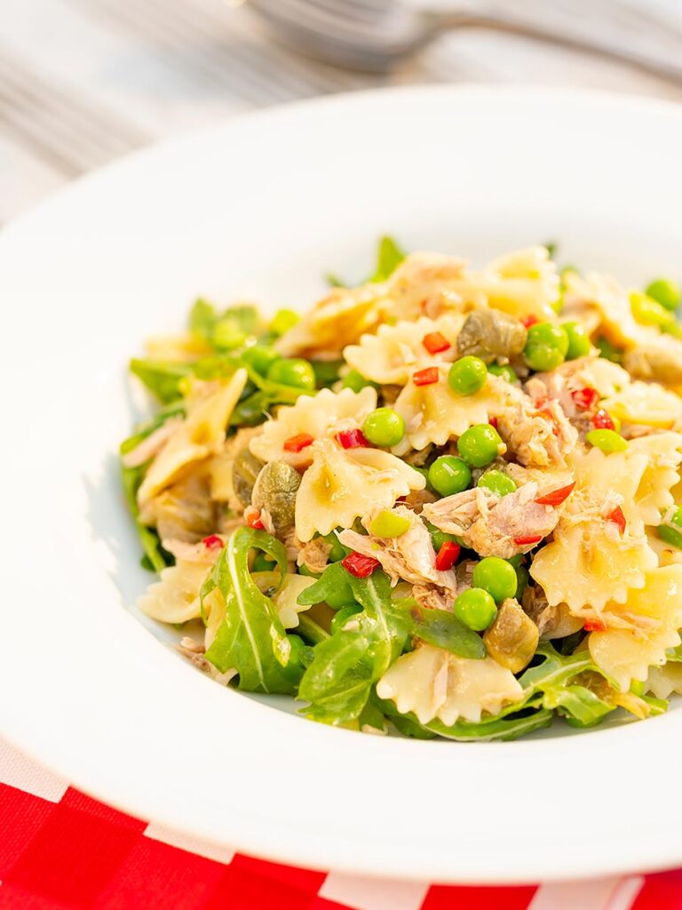 Portrait image of a tuna pasta salad with peas, chilli and rocket (arugula) served in a shallow white bowl