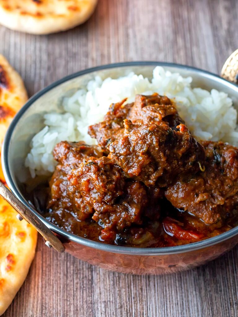 Portrait overhead image of a beef vindaloo curry in a copper coated curry bowl served with basmati rice and a naan bread