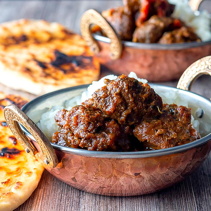 Square image of a beef vindaloo curry in a copper coated curry bowl served with basmati rice and a naan bread