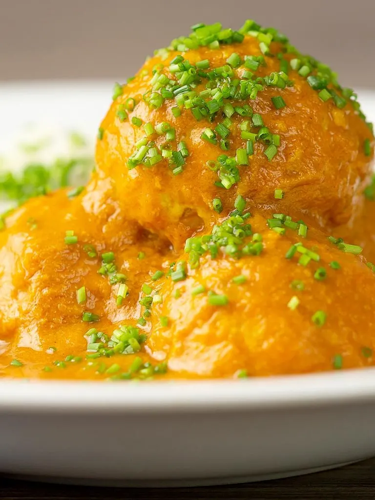 Portrait close up image of a chicken kofta or meatball curry in a masala sauce with snipped chives