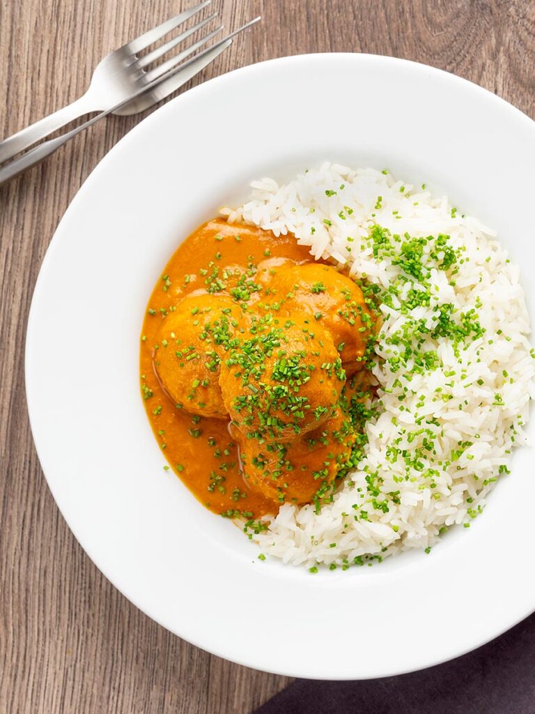 Portrait overhead image of a chicken kofta or meatball curry in a masala sauce with snipped chives