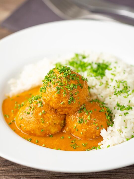 Portrait image of a chicken kofta or meatball curry in a masala sauce with snipped chives