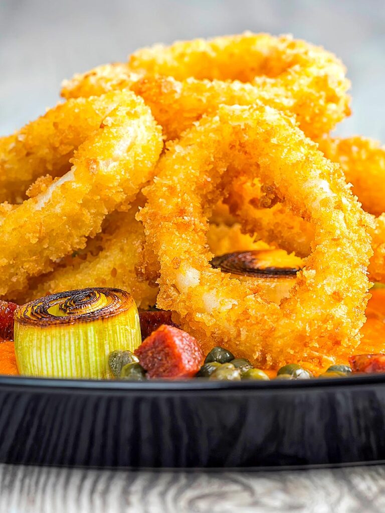 Portrait close up image of crispy fried calamari rings that are breaded and served with salami, leeks, and capers
