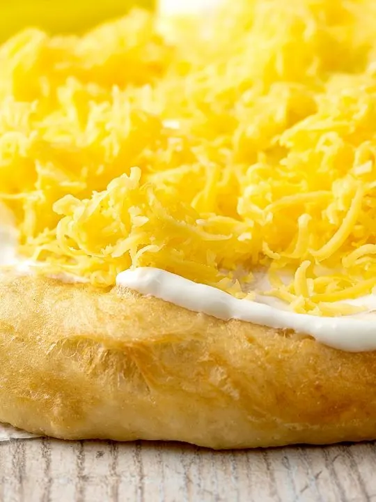 Portrait close up image of Hungarian fried bread or langos topped with sour cream and cheese