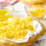 Portrait image of Hungarian fried bread or Langos topped with sour cream, cheese and garlic oil