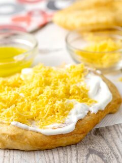 Portrait image of Hungarian fried bread or Langos topped with sour cream, cheese and garlic oil