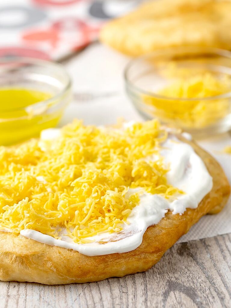 Portrait image of Hungarian fried bread or Langos topped with sour cream, cheese and garlic oil