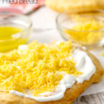 Portrait image of Hungarian fried bread or Langos topped with sour cream, cheese and garlic oil with text overlay