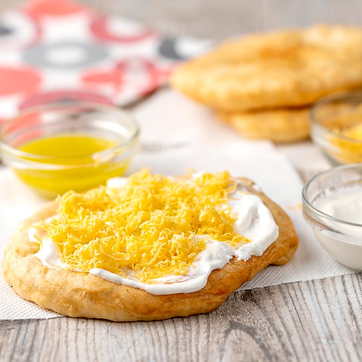 Square image of Hungarian fried bread or Langos topped with sour cream, cheese and garlic oil with text overlay