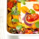 Portrait close up image of Mediterranean baked feta cheese with tomatoes and peppers served in a white gratin bowl