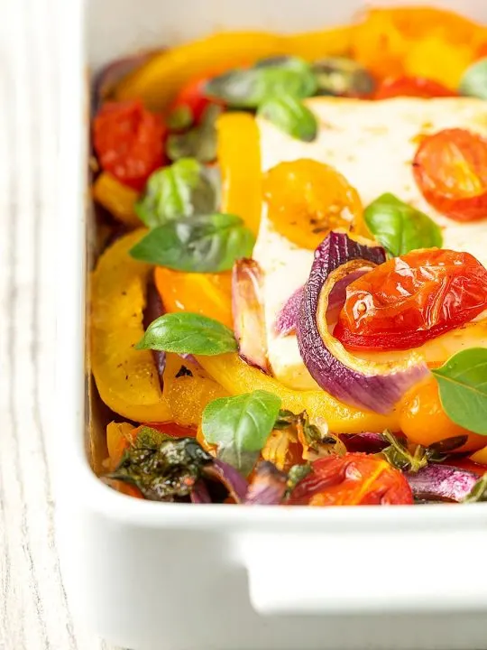 Portrait close up image of Mediterranean baked feta cheese with tomatoes and peppers served in a white gratin bowl