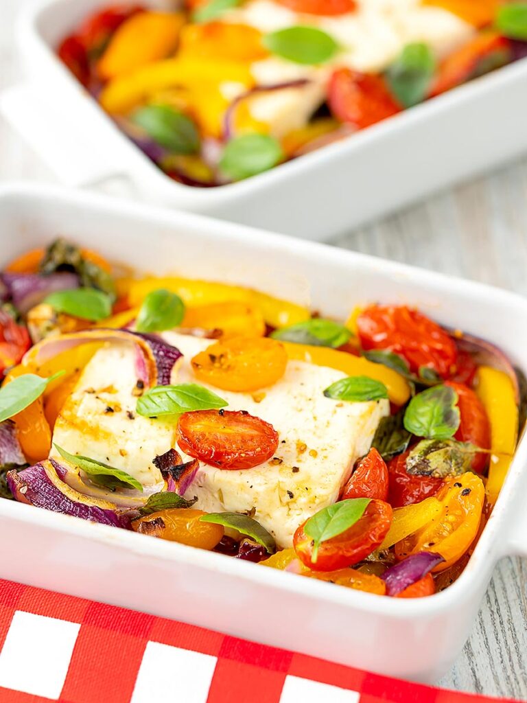 Portrait image of Mediterranean baked feta cheese with tomatoes and peppers served in a white gratin bowl