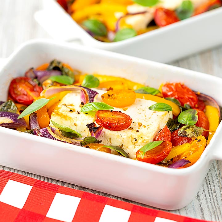 Square image of Mediterranean baked feta cheese with tomatoes and peppers served in a white gratin bowl