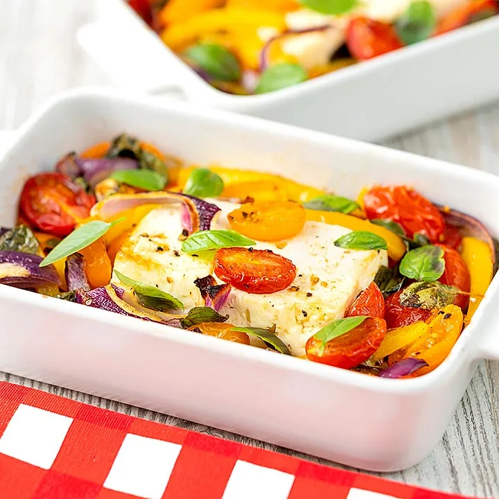 Square image of Mediterranean baked feta cheese with tomatoes and peppers served in a white gratin bowl