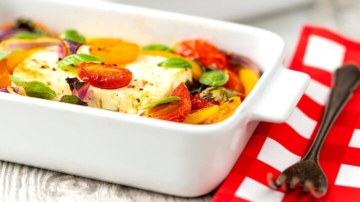 Landscape image of Mediterranean baked feta cheese with tomatoes and peppers served in a white gratin bowl