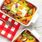Portrait image of Mediterranean baked feta cheese with tomatoes and peppers served in a white gratin bowl