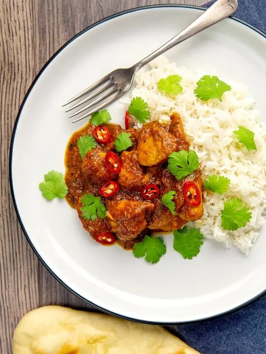 Portrait overhead image of a chicken pathia or patia curry served on a plate with rice, chilli slices and fresh coriander
