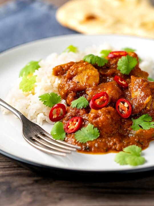 Portrait image of a chicken pathia or patia curry served on a plate with rice, chilli slices and fresh coriander