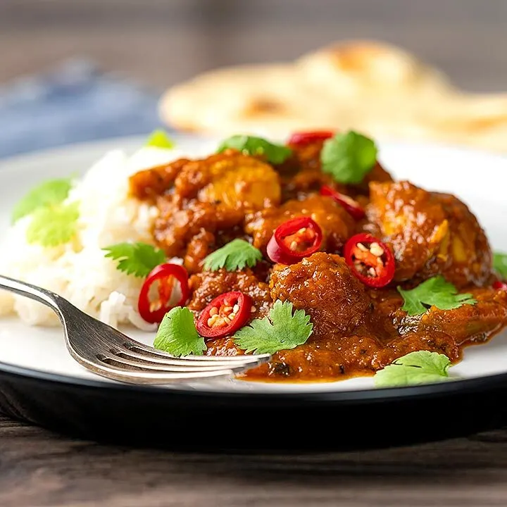 Square image of a chicken pathia or patia curry served on a plate with rice, chilli slices and fresh coriander