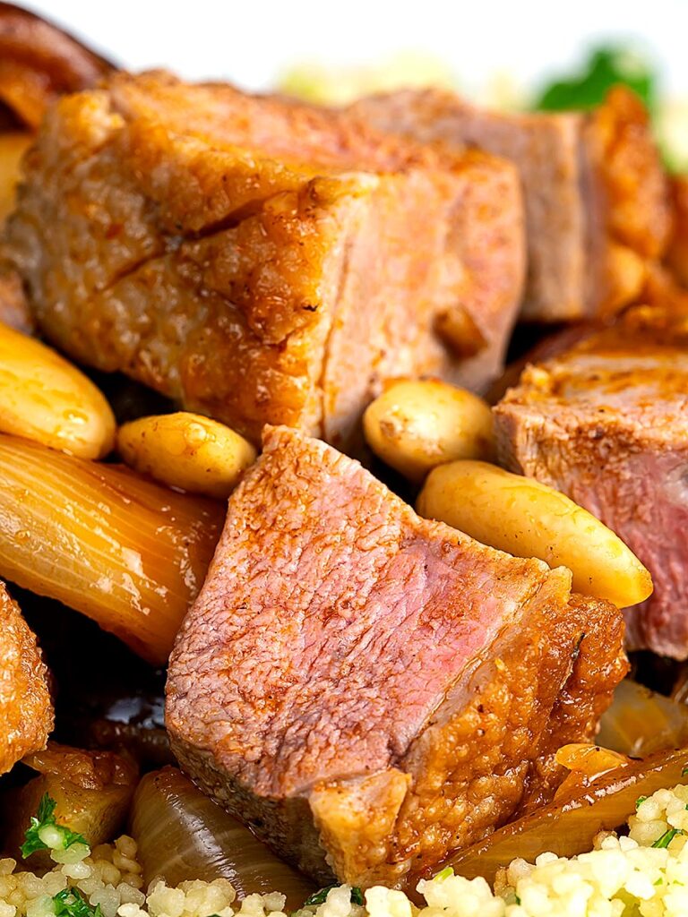 Portrait close up image of a duck breast tagine with dates and almonds served on a bed of buttered couscous