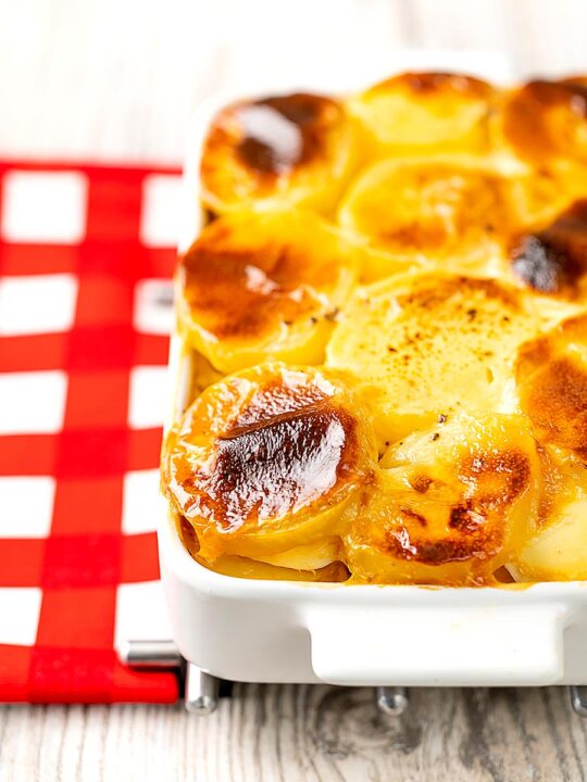 Portrait image of rakott krumpli or Hungarian layered potatoes served in a white gratin dish