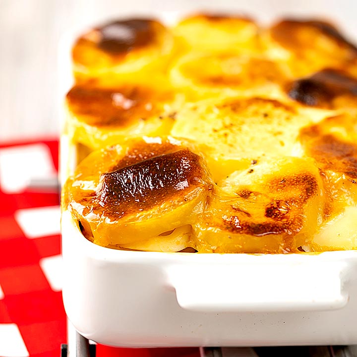 Square image of rakott krumpli or Hungarian layered potatoes served in a white gratin dish
