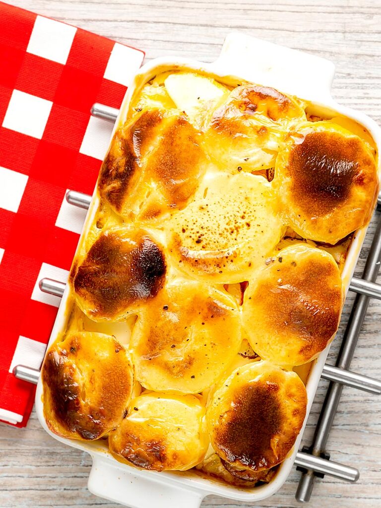 Portrait overhead image of rakott krumpli or Hungarian layered potatoes served in a white gratin dish