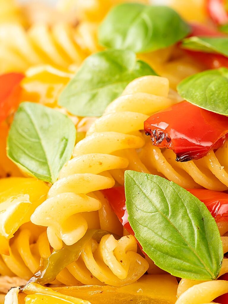 Portrait close up image of spicy chicken pasta made with fusilli and roasted peppers served with fresh basil leaves