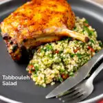 Portrait image of a herby tabbouleh salad served on a dark plate with a harissa glazed pork chop