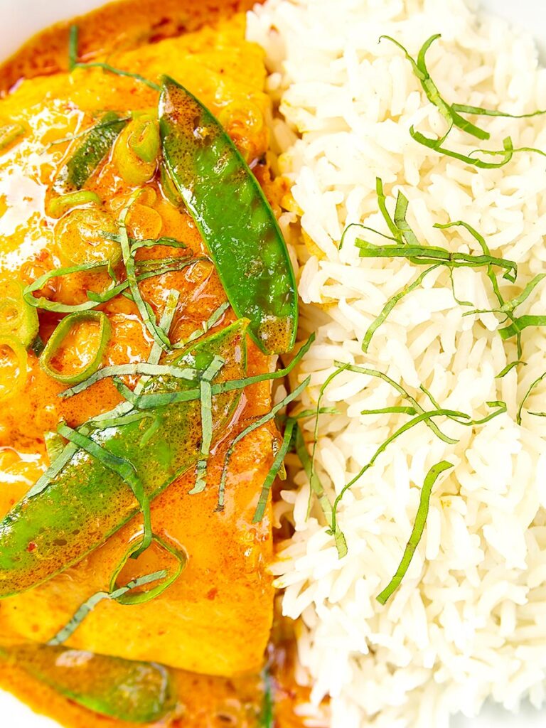 Portrait overhead close up image of a red Thai salmon curry with mangetout peas and shredded Thai basil served with jasmine rice