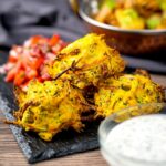 Portrait image of crispy air fryer onion bhaji or pakora served with a curry and mint and yoghurt dip
