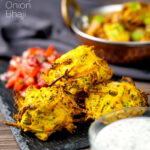 Portrait close up image of crispy air fryer onion bhaji or pakora served with a curry and mint and yoghurt dip featuring a text overlay