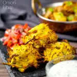 Portrait close up image of crispy air fryer onion bhaji or pakora served with a curry and mint and yoghurt dip featuring a text overlay