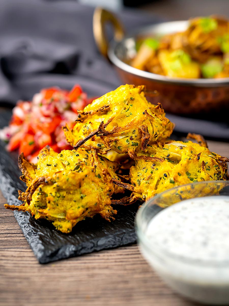 Portrait image of crispy air fryer onion bhaji or pakora served with a curry and mint and yoghurt dip