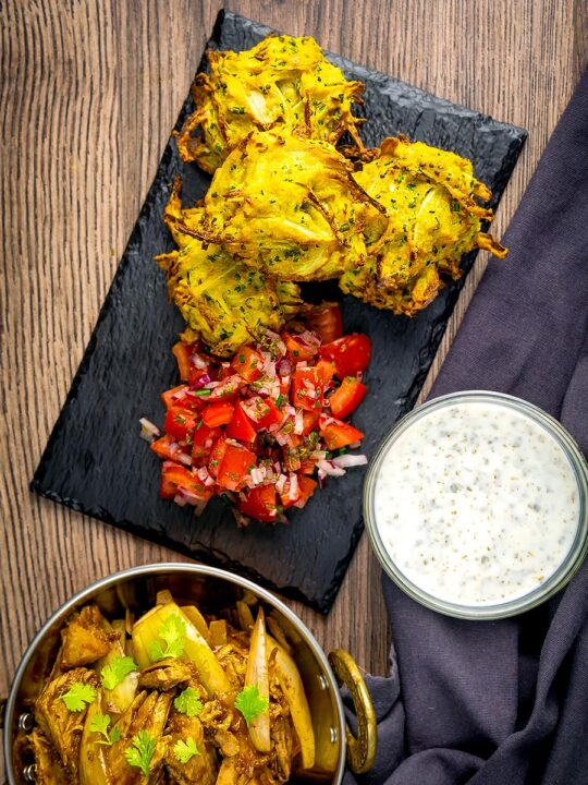 Portrait overhead image of crispy air fryer onion bhaji or pakora served with a curry and mint and yoghurt dip