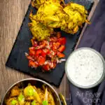 Portrait overhead image of crispy air fryer onion bhaji or pakora served with a curry and mint and yoghurt dip featuring a text overlay