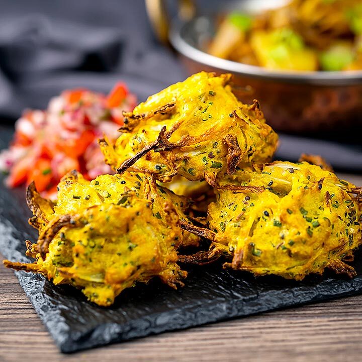 Square image of crispy air fryer onion bhaji or pakora served with a curry and mint and yoghurt dip