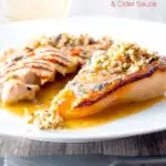 Portrait image of a savoury baked pears side dish in a cider sauce served on a white plate with text overlay