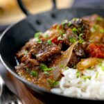 Portrait image of an onion rich beef dopiaza curry served in an iron karahi with rice and a coriander garnish