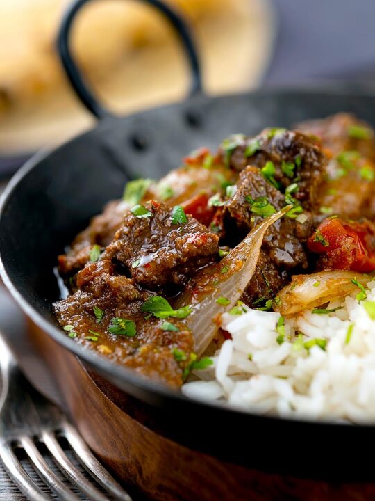 Portrait image of an onion rich beef dopiaza curry served in an iron karahi with rice and a coriander garnish