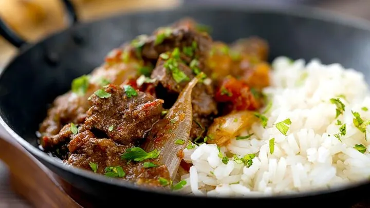 Landscape image of an onion rich beef dopiaza curry served in an iron karahi with rice and a coriander garnish