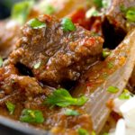 Portrait close up image of an onion rich beef dopiaza curry served in an iron karahi with rice and a coriander garnish