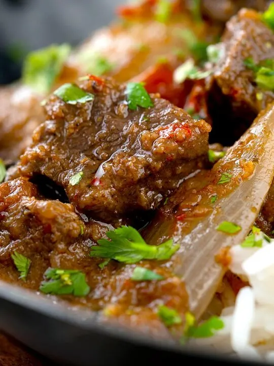 Portrait close up image of an onion rich beef dopiaza curry served in an iron karahi with rice and a coriander garnish
